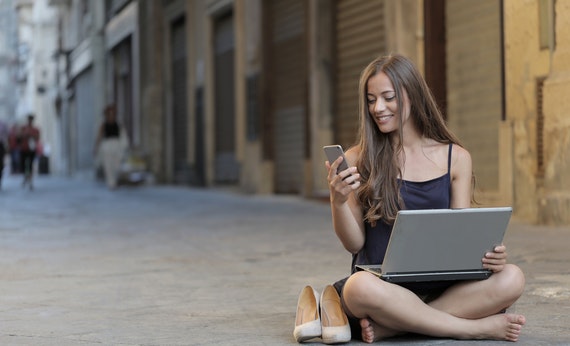 Wanita menggunakan laptop dan smartphone sambil duduk bersila ditengah jalan